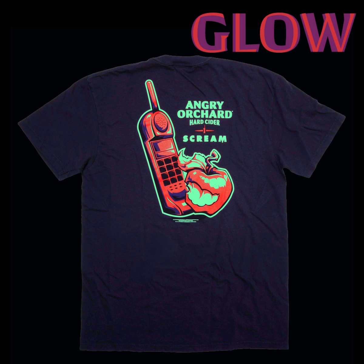 A black t-shirt shown from the back, featuring a large graphic print of a red cordless phone and a red apple with green glowing details, alongside the text 'ANGRY ORCHID BASKET COFFEE SCREAM'. The word 'GLOW' is written in a glowing pink and purple font at the top of the image against a black background.
