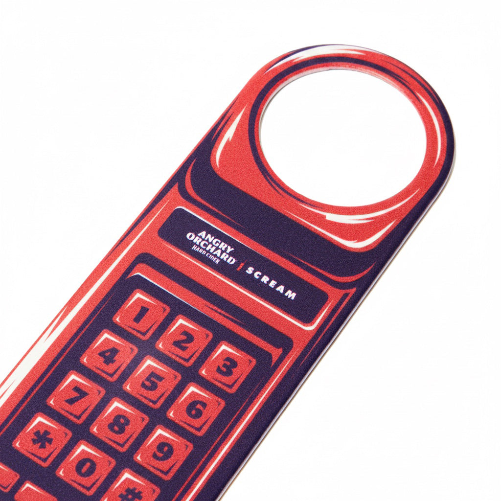 A stylized red and dark purple bottle opener with a circular cutout at the top and printed numbers, shown on a plain white background. Visible text reads 'ANGRY ORCHARD' and 'Scream'.