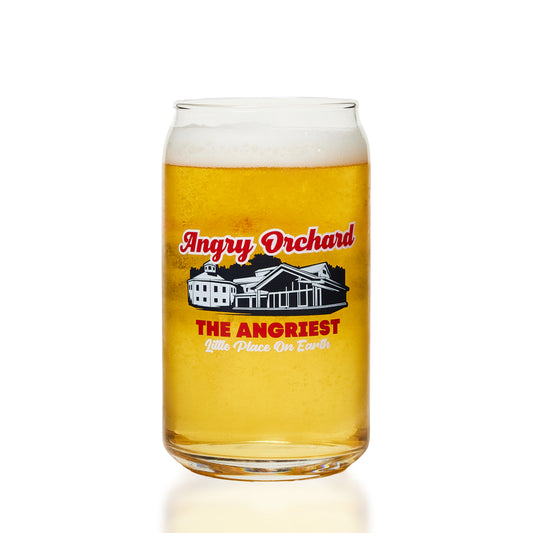 A clear glass can-shaped pint glass filled with golden cider and topped with white foam, featuring a printed Angry Orchard logo and house illustration on the front, set against a clean white background.
