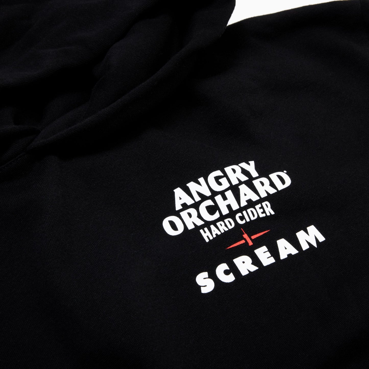 Close-up of a black hoodie featuring a white and red graphic print that reads 'ANGRY ORCHARD HARD CIDER SCREAM'.