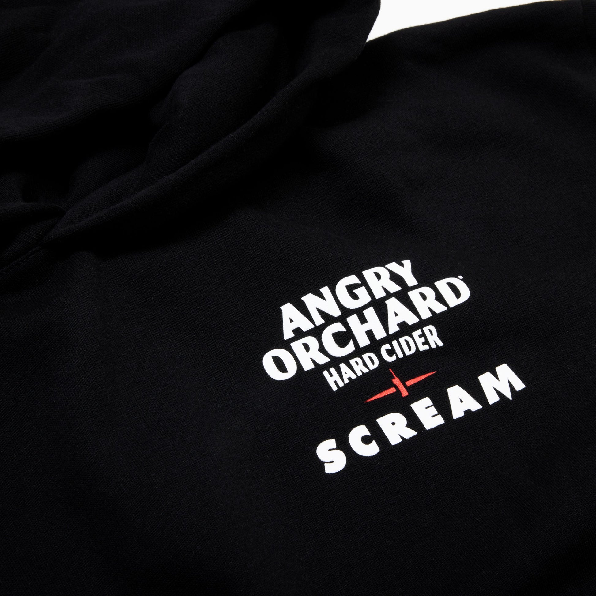 Close-up of a black hoodie featuring a white and red graphic print that reads 'ANGRY ORCHARD HARD CIDER SCREAM'.