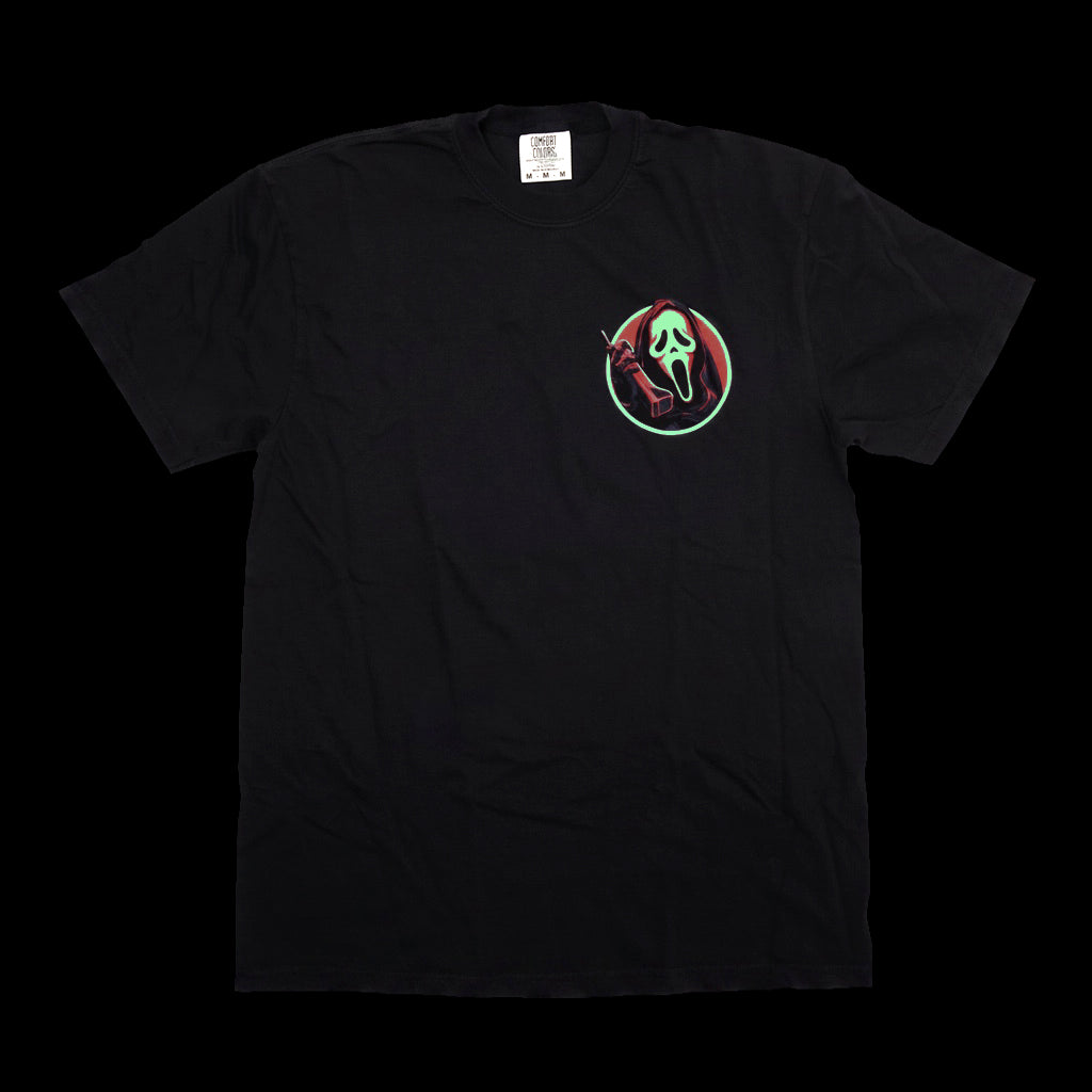 A black short-sleeve crewneck t-shirt featuring a circular chest graphic of a red devil figure and a green Ghostface mask inside a circle, displayed against a solid black background.